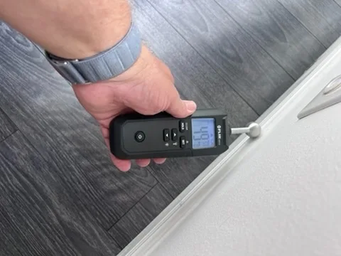 FLIR moisture meter taking a pinless reading along a baseboard and trim during a mold inspection