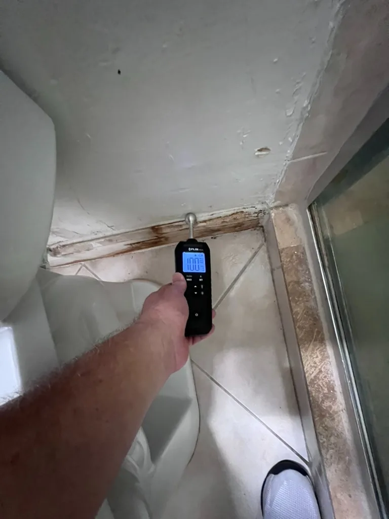 FLIR moisture meter reading a bathroom corner with visible staining near a shower enclosure
