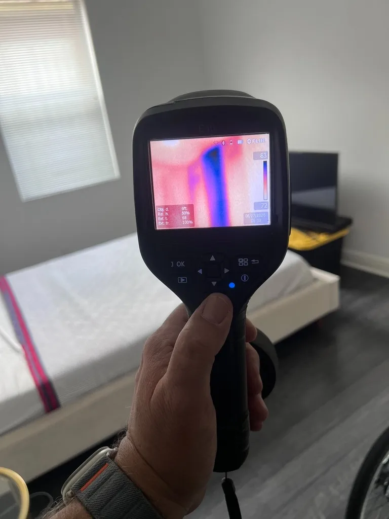 Home Enviro inspector using a FLIR infrared thermal imaging camera to scan a bedroom wall for hidden moisture