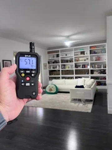 FLIR thermo-hygrometer reading temperature and humidity in a living room with built-in shelving