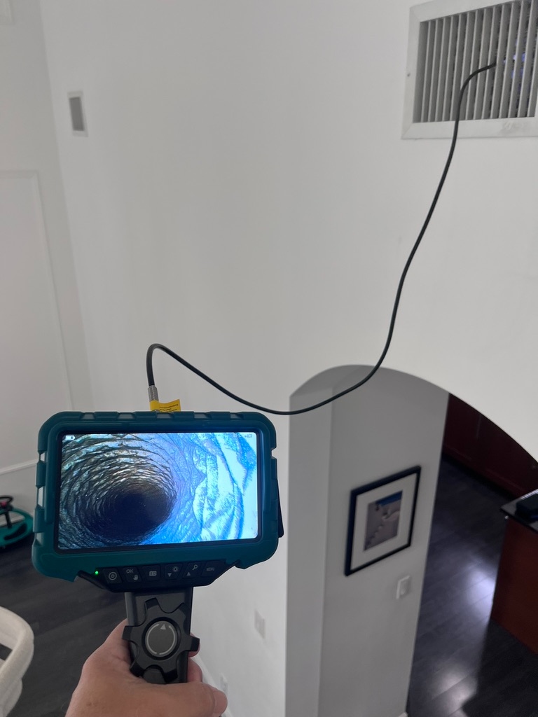 Inspector using a borescope camera to inspect inside an air duct, with the live camera feed showing the duct interior