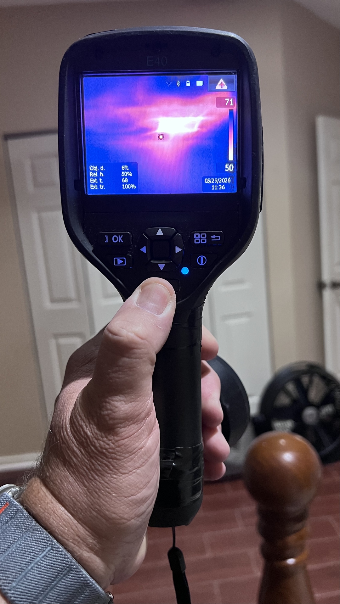 Licensed inspector holding a FLIR thermal imaging camera showing a heat signature on a ceiling during a real inspection