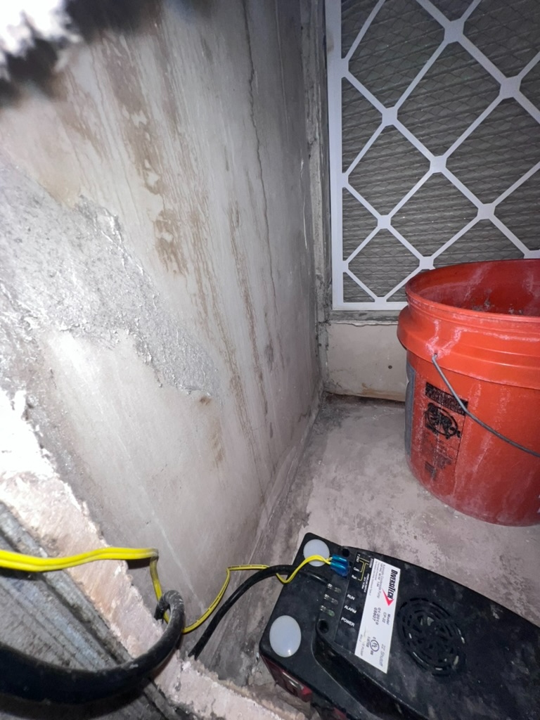 Air handler closet showing standing water along the base wall with an active remediation pump and filter unit during a mold investigation