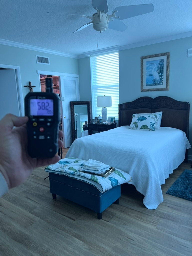 FLIR humidity meter held in a residential bedroom showing a reading of 58.2 percent relative humidity during an indoor air quality assessment